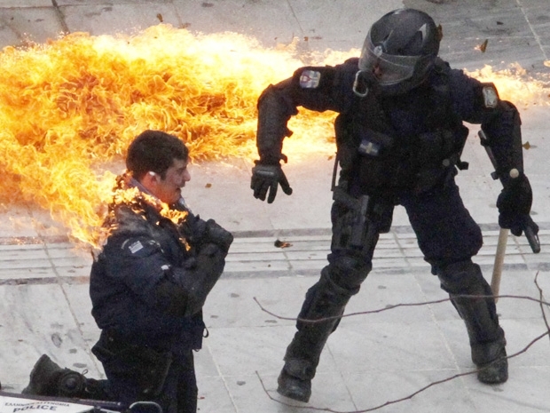 Um policial  atingido pelas chamas e seu colega tenta ajud-lo. Bomba foi jogada por manifestantes nesta quarta-feira