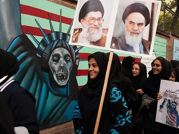 Mulheres passam por faixa que mostra a Esttua da Liberdade com uma caveira no lugar do rosto, em Teer
