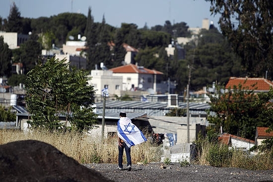 Jovem enrolado em bandeira israelense participa de parada pelo Dia de Jerusalm; em Jerusalm Oriental