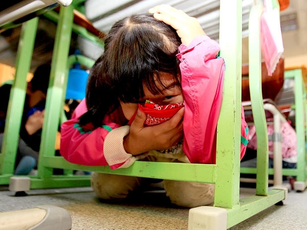 Menina se protege embaixo de mesa em sala de aula durante simulao de terremoto